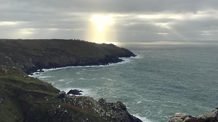 Photo showing sunbeams breaking through cloud over a rugged coastline